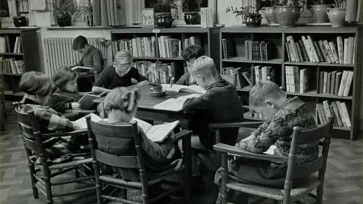 Kinderen lezen boek aan tafel in kinderleeszaal / jeugdbibliotheek. [1935].  fotograaf: Wiel van der Randen